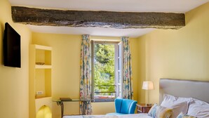 A hotel room with a bed, a chair, a window with curtains, a TV mounted on the wall, and a small table with a lamp. - Double Room with Wi-Fi and Air Conditioning (Cagnes-sur-Mer)