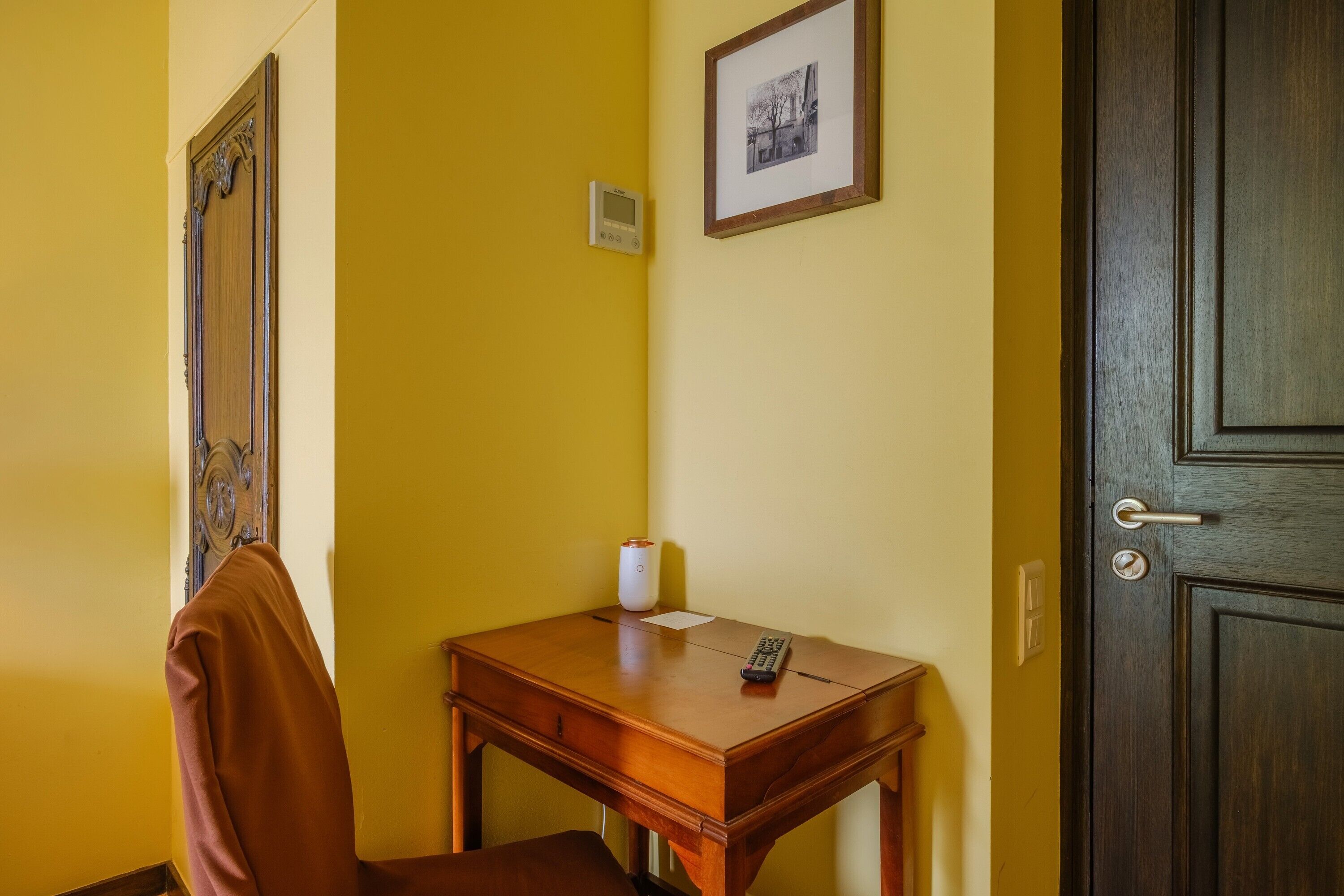 A room with a wooden desk, a chair, a framed picture on the wall, and a door.