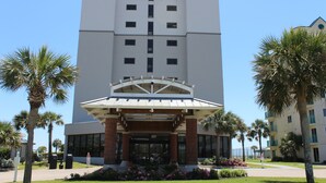 A multi-story hotel with a central entrance, palm trees, and a clear sky. - Couples Coastal Retreat 1min walk to the beach! (Gulf Shores)