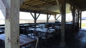 An outdoor covered dining area with wooden tables and chairs, a bar, and a view of the beach. - Couples Coastal Retreat 1min walk to the beach! (Gulf Shores)
