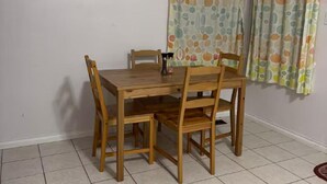 Ein Esstisch mit vier Holzstühlen, einer kleinen Tischlampe und einem gemusterten Vorhang im Hintergrund.
