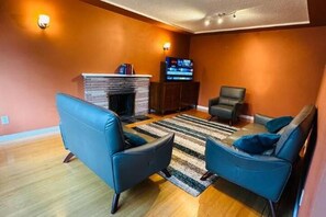 A living room with a fireplace, two blue sofas, a TV, and a striped rug. - Gather House Vancouver (Vancouver)
