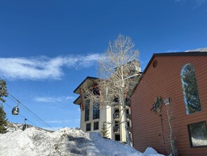 A building with multiple windows and balconies, a tree in front, and a clear blue sky. - Village Living at Helios (Mammoth Lakes)