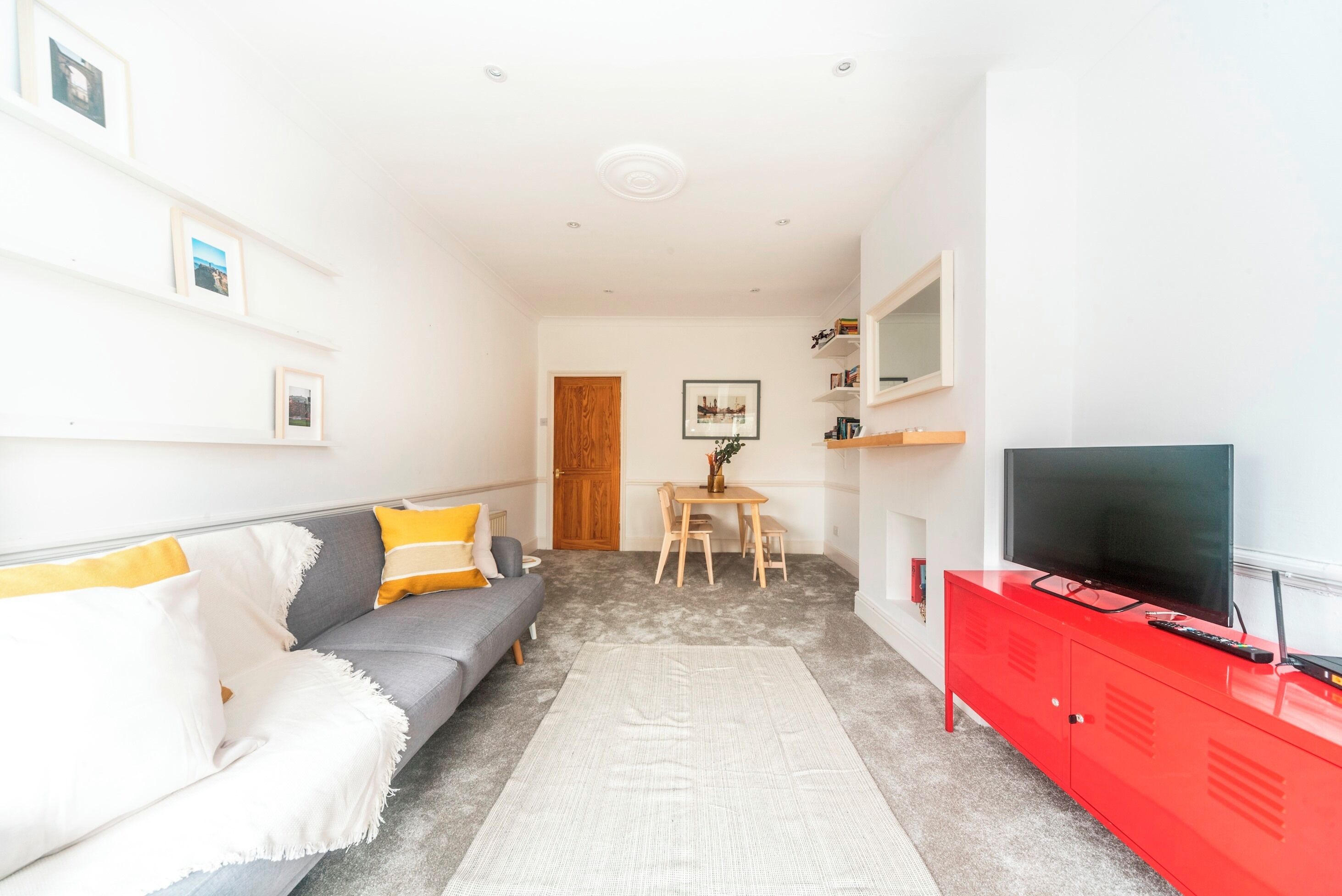 Un salon moderne avec un canapé gris, un meuble rouge et un téléviseur à écran plat.