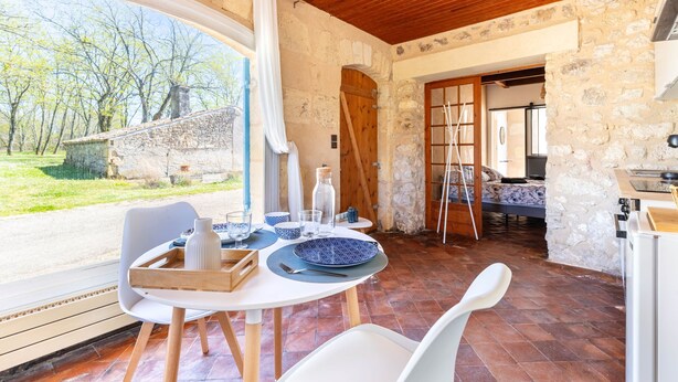 A dining area with a table set for two, a stone wall, and a view of the outdoors. - Domaine des Bruyères | Workshop (Saint-Savin)