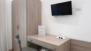 Um quarto pequeno com uma escrivaninha de madeira, uma cadeira, uma televisão e um frigorífico.