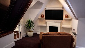A cozy room with a fireplace, a flat-screen TV, a brown armchair, and a potted plant. - THE GEORGIA ROSE - A southern charm, with lots of character! (Atlanta)