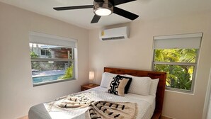 Een slaapkamer met een bed, een plafondventilator, twee ramen met uitzicht en een airconditioning.