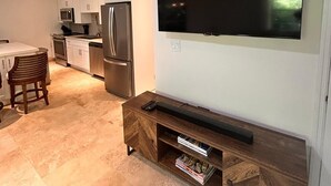 Een moderne keuken met witte kasten, roestvrijstalen apparatuur en een flatscreen televisie aan de muur.