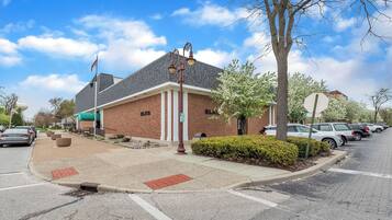 A brick building with a flagpole, a parking lot, and a street with cars.