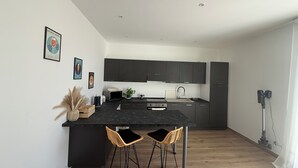 A modern kitchen with dark cabinets, a black countertop, and two wicker bar stools. - Casa Lo Bianco sea view apartment in Terrasini (Terrasini)