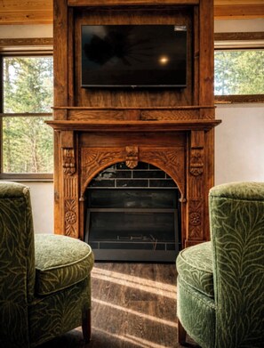 A fireplace with a TV above it, flanked by two upholstered chairs. - Secluded Creekside Cabin in Bailey With Private Hot Tub and Steam Room. (Bailey)