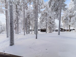 A snow-covered landscape with tall trees and a cabin in the background. - Kelokaltiokylä mökki 58 by Interhome (Kuusamo)