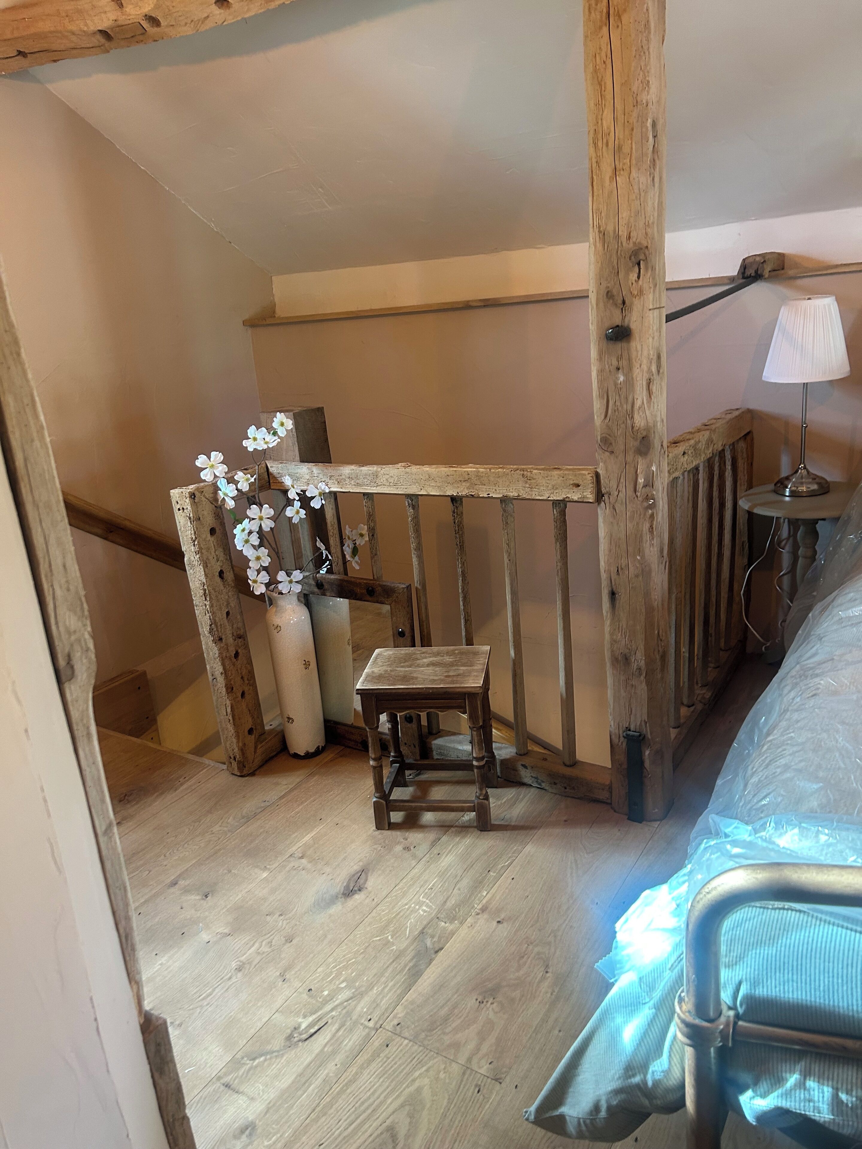 Ein rustikales Schlafzimmer im Dachgeschoss mit einem kleinen Holzschemel, einer Vase mit Blumen und einer Lampe auf einem Tisch.
