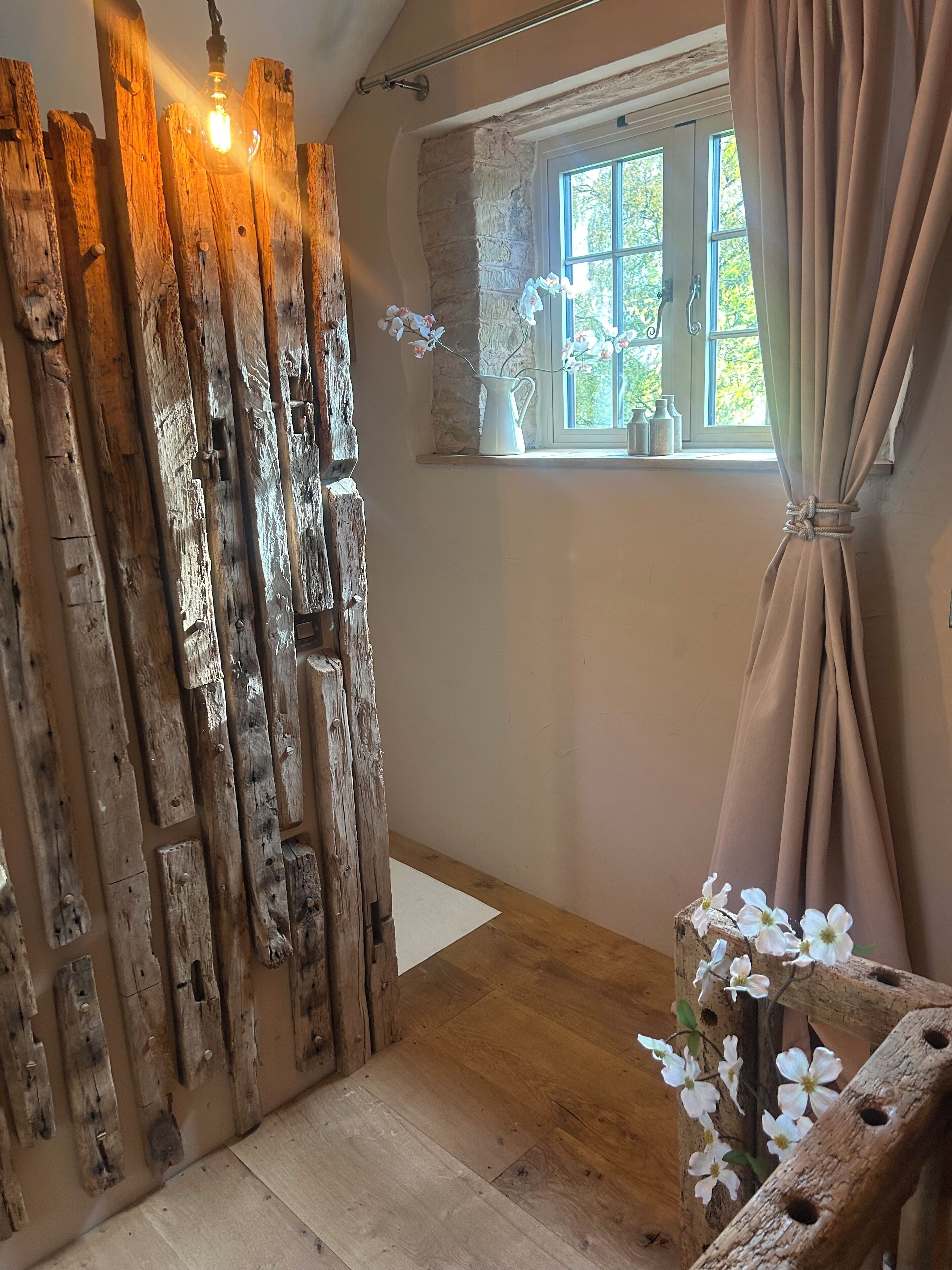 A rustic room with a wooden wall, a window with curtains, and a wooden floor.