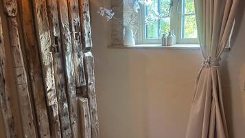 A rustic room with a wooden wall, a window with curtains, and a wooden floor.