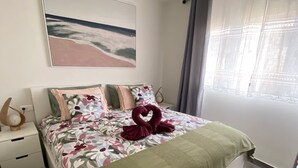 Una camera da letto con un letto, un comodino, una lampada, un quadro appeso e una finestra con tende.