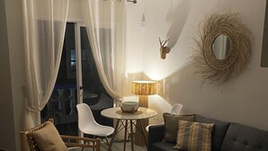 Un accogliente soggiorno con un divano scuro, una poltrona in legno, un tavolino tondo con una lampada e tende leggere.