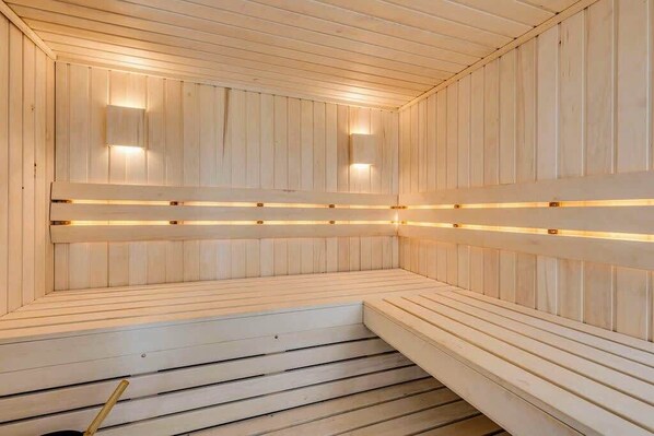 A sauna with wooden walls and benches, equipped with wall-mounted lights. - Acreage, Hot Tub, AC, Pool Table, Sauna, King Beds (Airdrie)