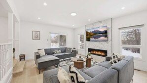 A modern living room with a grey sofa set, a fireplace, and a large TV mounted on the wall.