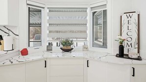 A kitchen with white cabinets, a marble countertop, and a bay window with open shutters.