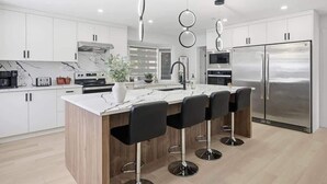 A modern kitchen with white cabinets, a marble countertop, and a stainless steel refrigerator.