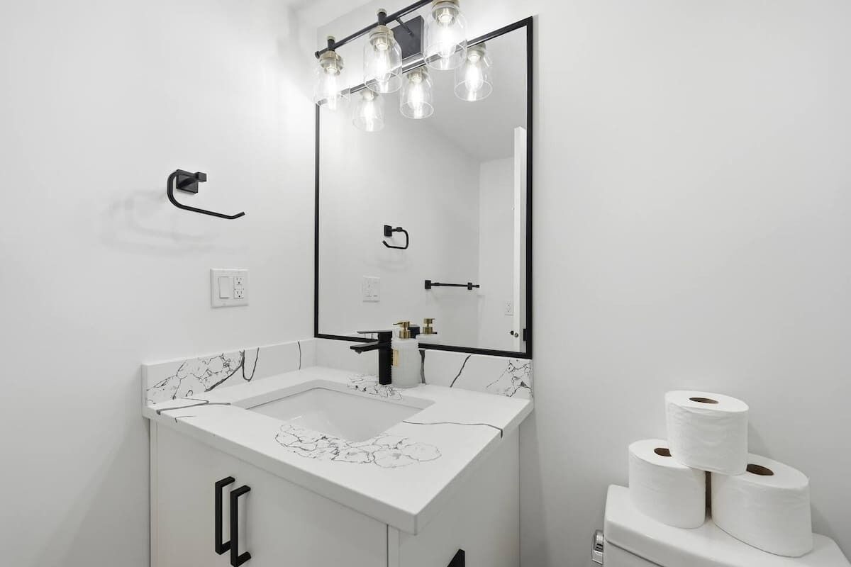Un baño moderno con lavamanos de mármol blanco, un espejo grande y un dispensador de papel higiénico.