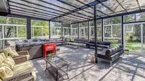 A covered outdoor area with seating, a hot tub, and large windows.