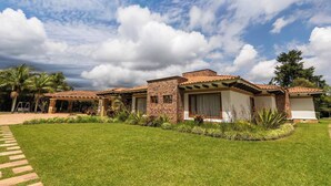 A two-story house with a brick facade, a tiled roof, and a well-maintained lawn. - Mansión de lujo “La Reina” Llanogrande (Rionegro)