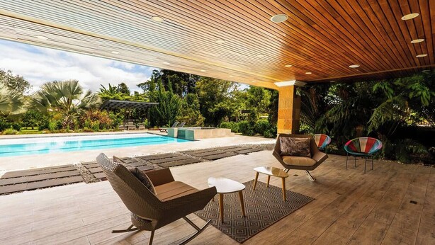 A covered outdoor area with a pool, wooden flooring, and seating arrangements. - Mansión de lujo “La Reina” Llanogrande (Rionegro)