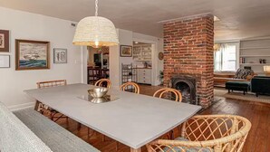 Comedor con una mesa grande, sillas, lámpara colgante y chimenea de ladrillo.