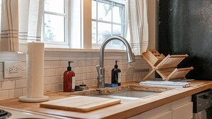 Una cocina con un lavamanos de acero inoxidable, encimeras de madera, una estufa y una ventana con cortinas.