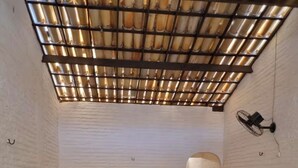 Una habitación pequeña y estrecha con dos camas de madera, un techo inclinado con estructura similar a bambú y un ventilador de pared.