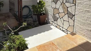 Un área de patio techada con pared de piedra, techo de baldosas y plantas en macetas.