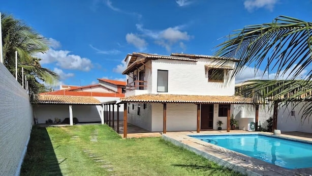 Una casa de dos pisos con piscina, un patio cubierto y un césped bien cuidado.