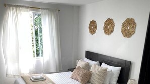 Een slaapkamer met een bed, nachtkastjes, een stoel en een raam met gordijnen.