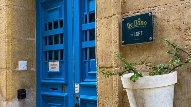 Une porte bleue avec une enseigne indiquant « De Bono Holiday Apartments The LOFT » et un jardinier contenant une petite plante.