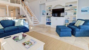 A spacious living room with a staircase, a TV, and a bookshelf. - Aloha from Kure South (Kure Beach)