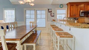 A kitchen with wooden cabinets, a granite countertop, and a dining area with a wooden table and benches. - Aloha from Kure South (Kure Beach)