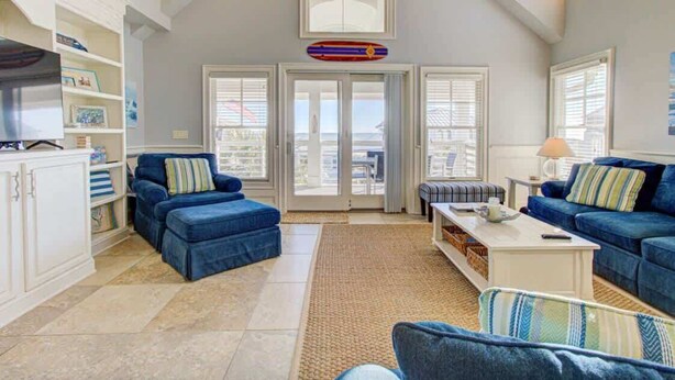 A spacious living room with a high ceiling, large windows, and a view of the city. - Aloha from Kure South (Kure Beach)