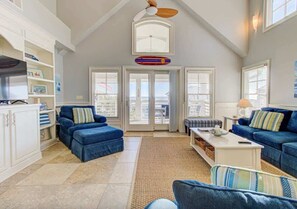 A spacious living room with a high ceiling, large windows, and a view of the city. - Aloha from Kure South (Kure Beach)