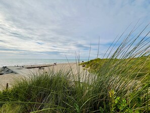 En strand med en sanddyn i förgrunden, en sandstrand och havet i bakgrunden.