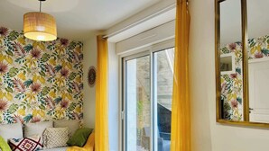 Um quarto com parede estampada, uma mesa redonda, um sofá com almofadas, uma luminária pendente e uma porta de vidro deslizante.