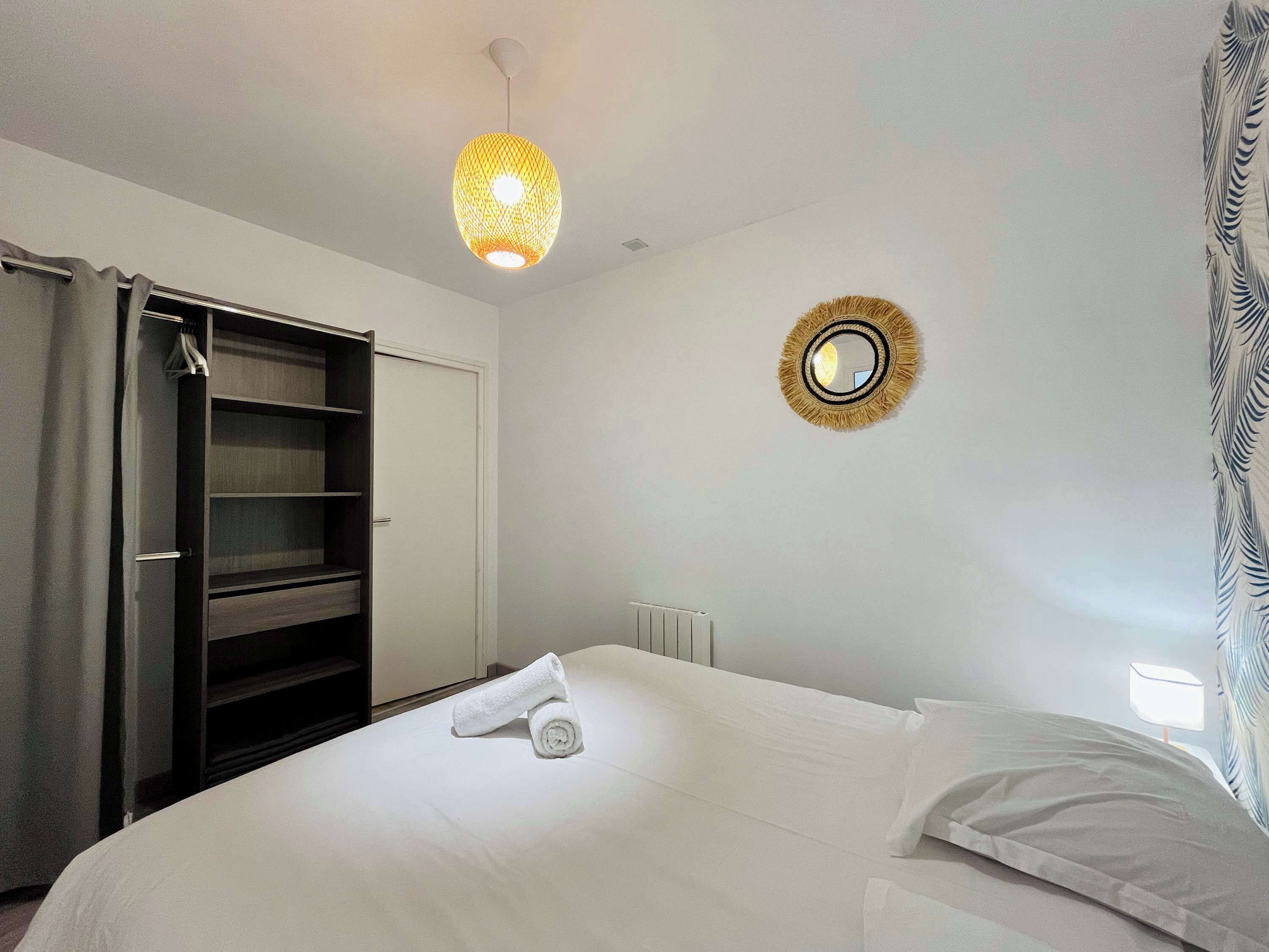 Een slaapkamer met een bed, een garderobe, een spiegel en een hanglamp.