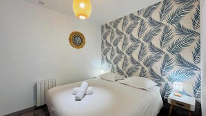 Quarto de hotel com cama, luminária fixada na parede, um ornamento na parede e mesa de cabeceira com abajur.