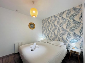 Une chambre d’hôtel comprenant un lit, un luminaire fixé au mur, un élément décoratif mural et une table de chevet avec une lampe.