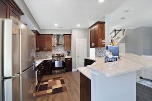 A modern kitchen with dark wooden cabinets, a stainless steel refrigerator, a built-in oven, and a marble countertop.