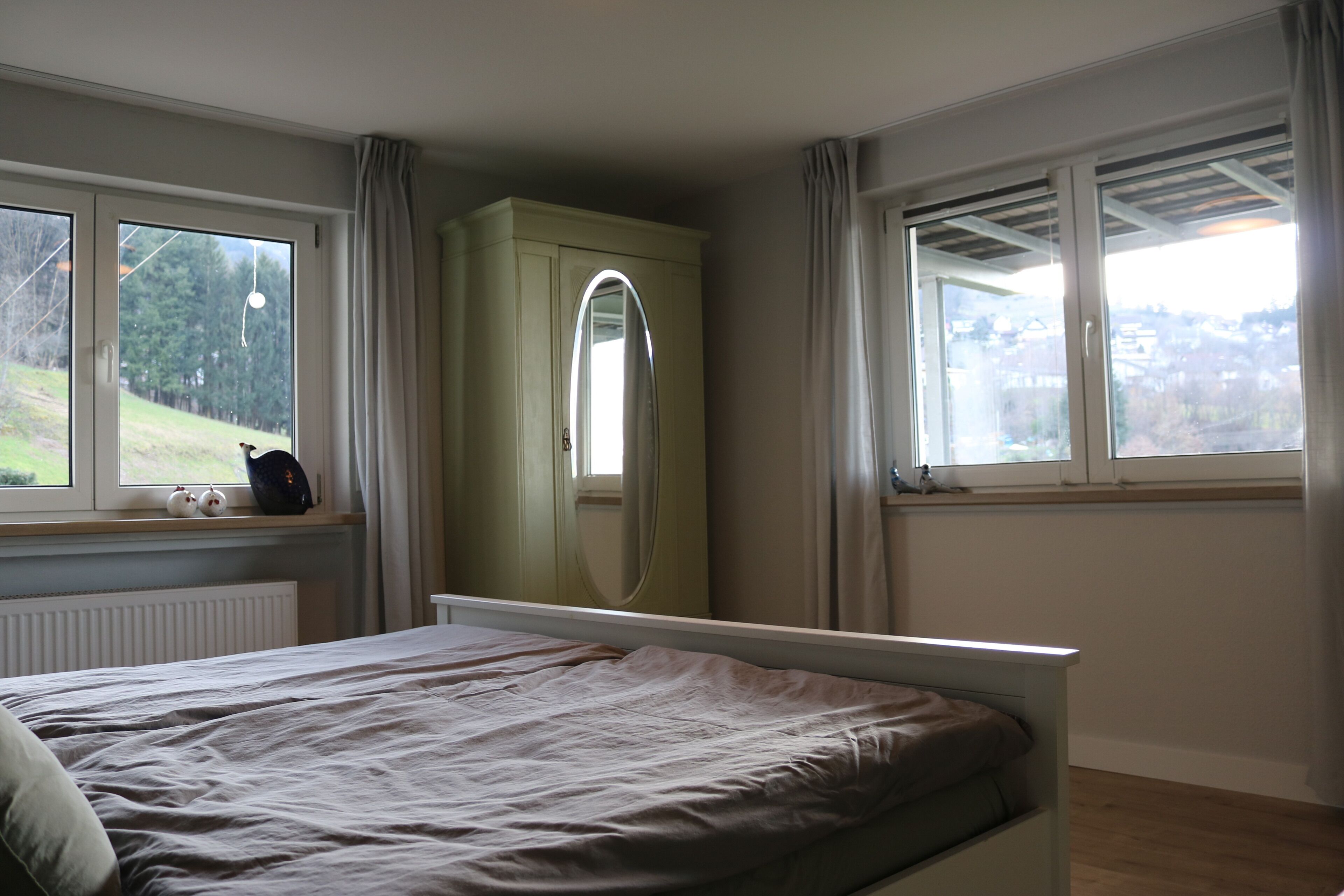 Een slaapkamer met een bed, een kledingkast, een raam met gordijnen en uitzicht op het omliggende landschap.
