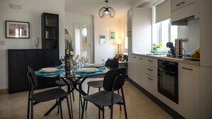 A modern kitchen with a dining area, featuring a glass-top table, black chairs, and a pendant light. - Rosie - Two Bedroom Apartment (Pietà)