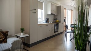 A modern kitchen with a central island, built-in appliances, and a dining area with a table and chairs. - Rosie - Two Bedroom Apartment (Pietà)